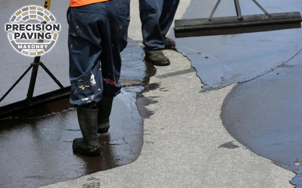 Image of two men applying seal coating to a driveway, illustrating the topic of seal coating cost in the accompanying blog.