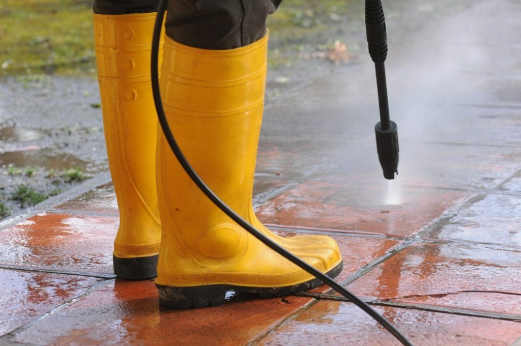 a man power washing and showing how to remove moss from pavers